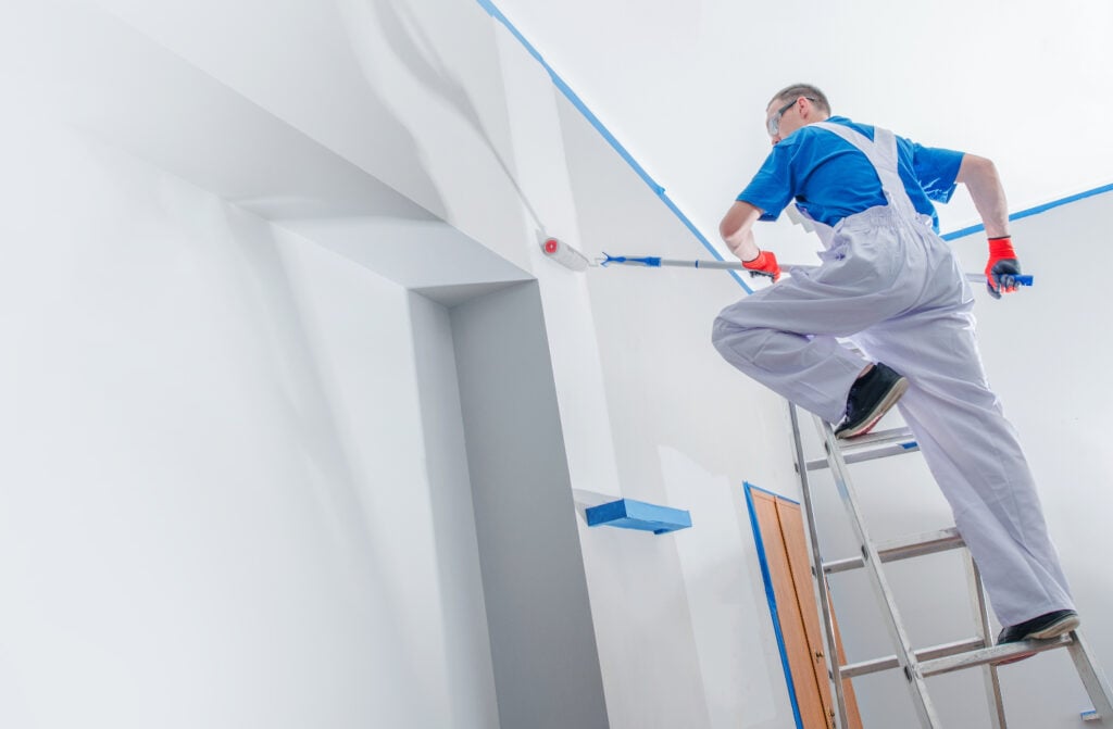 A painter stands on a ladder, painting a tall pillar white, carefully applying an even coat to transform its appearance