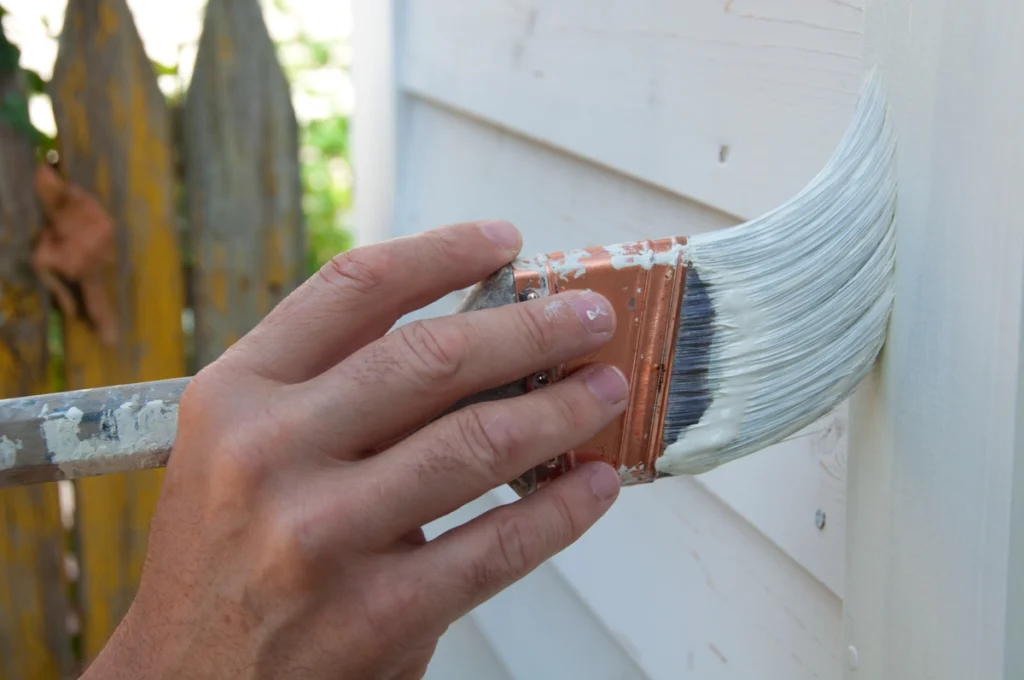 painter applying waterproof paint on siding