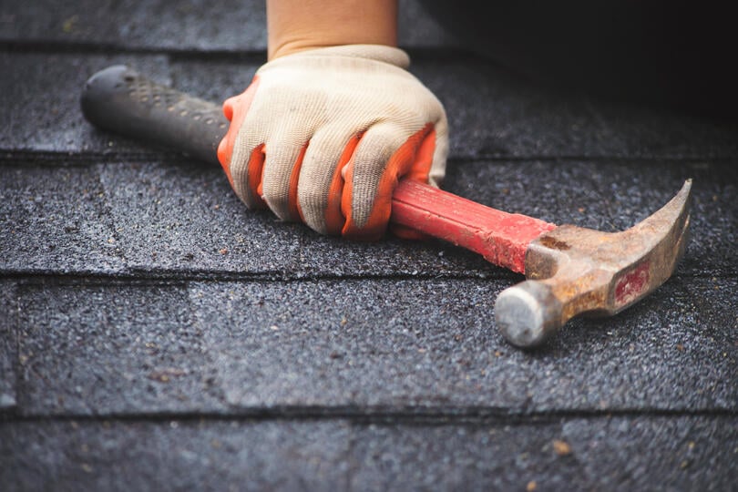 roofing tools-gloved hand holding a hammer on shingles
