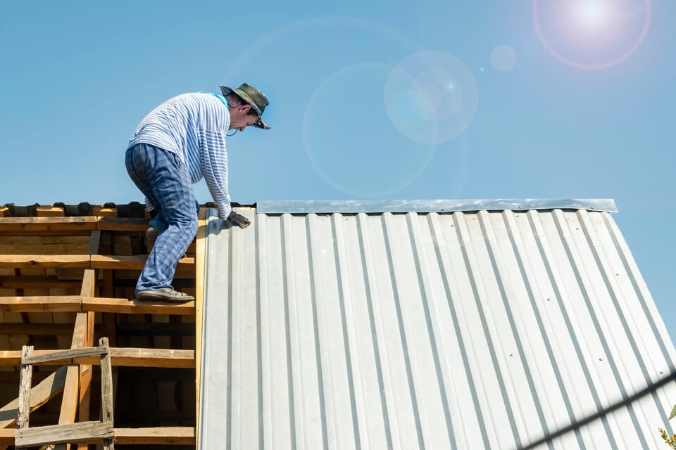 cost of metal roof vs shingle-man installing white metal roofing on a house roof