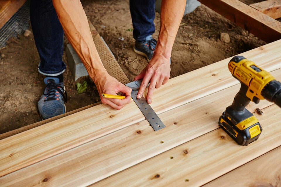how to build a deck-close up of hands measuring deck boards during construction