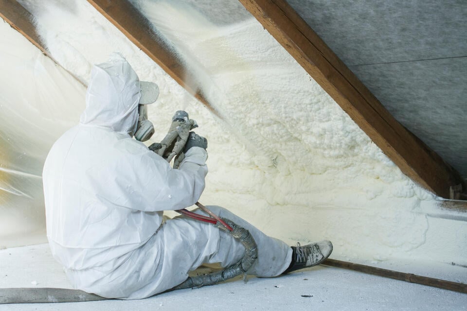 roof insulation-man in protective gear installing spray foam in an attic