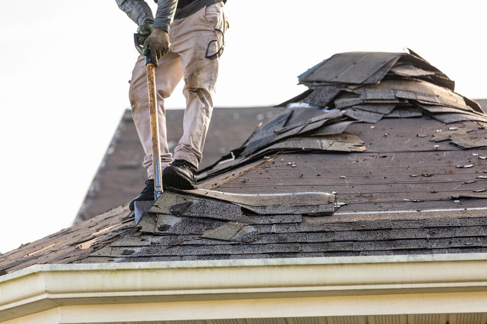 roof tear off-man using a shovel to remove old shingles from a roof