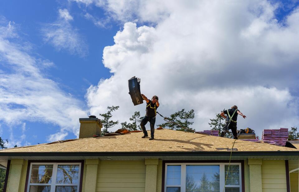 roof tear off-two roofers removing old roofing materials from a yellow house