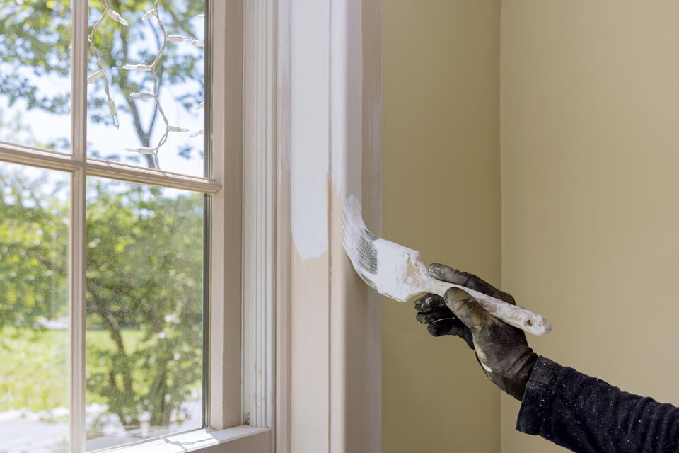 can you paint vinyl windows-close up of a gloved hand painting the interior part of a window frame white