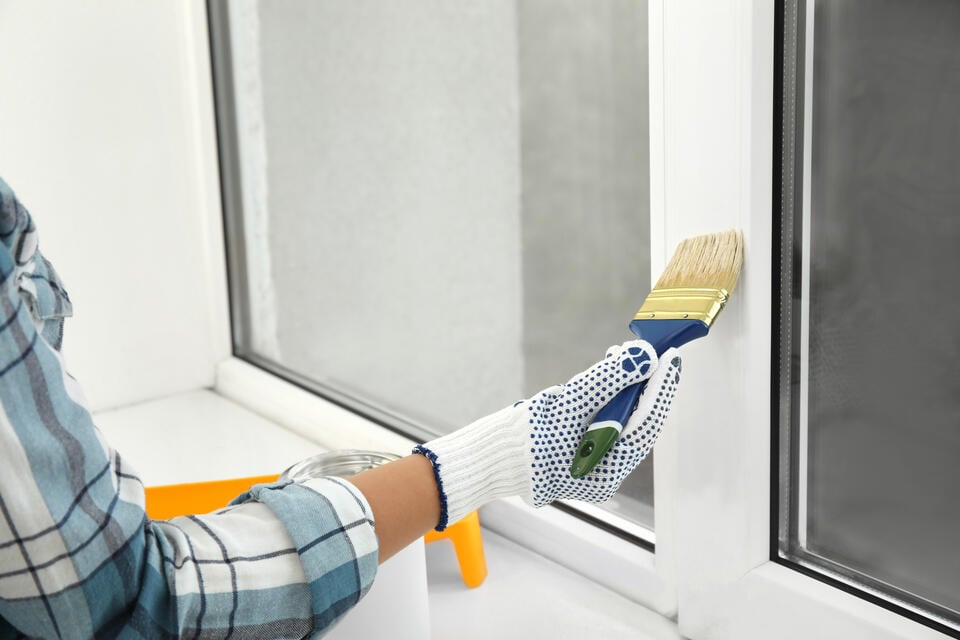 can you paint vinyl windows-close up of a gloved hand painting window frame white