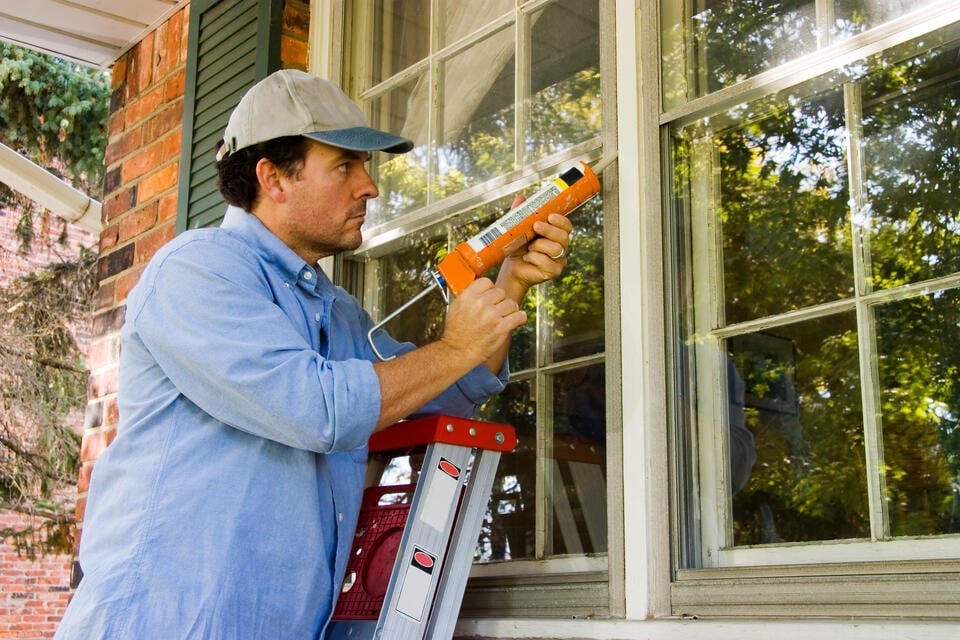 window seal repair-exterior view of man on ladder resealing window