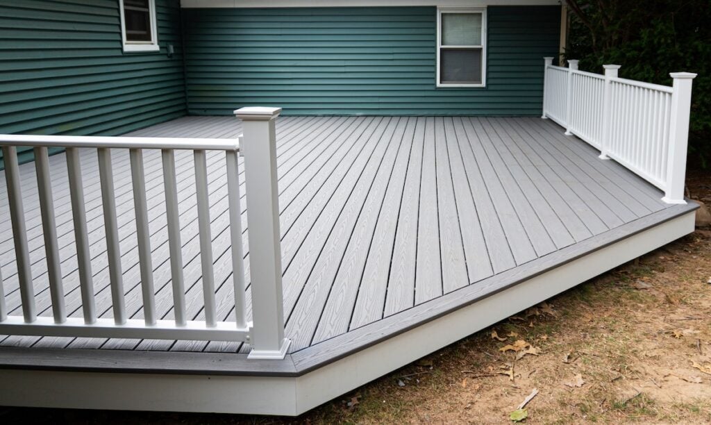 New composite deck on the back of a house with green vinyl siding.with whie railings.