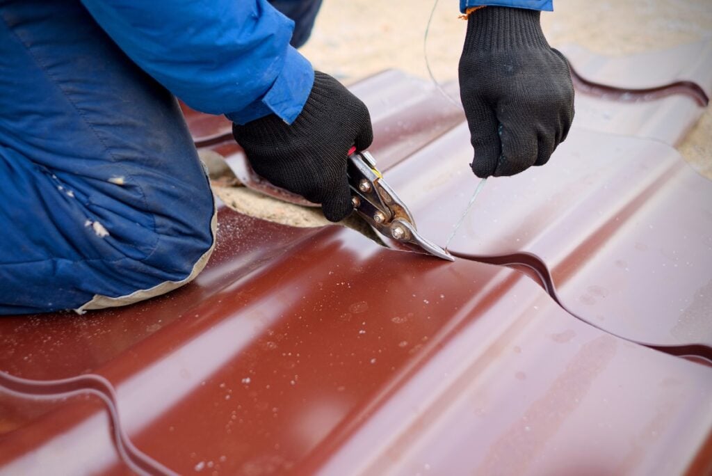 Worker use tin snips for cutting of metal roofing sheet.