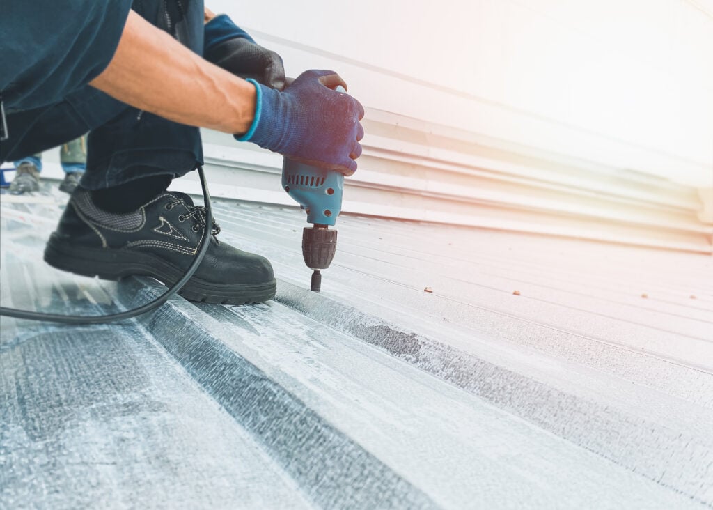 Workers wearing protective gear are screwing nuts on the metal roof with electric drills to install or repair with professional expertise