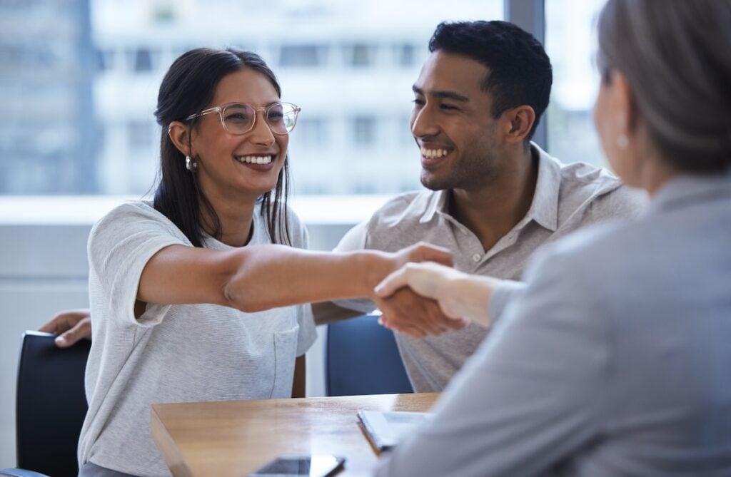 Shot of a young couple sharing a handshake with an adjuster.