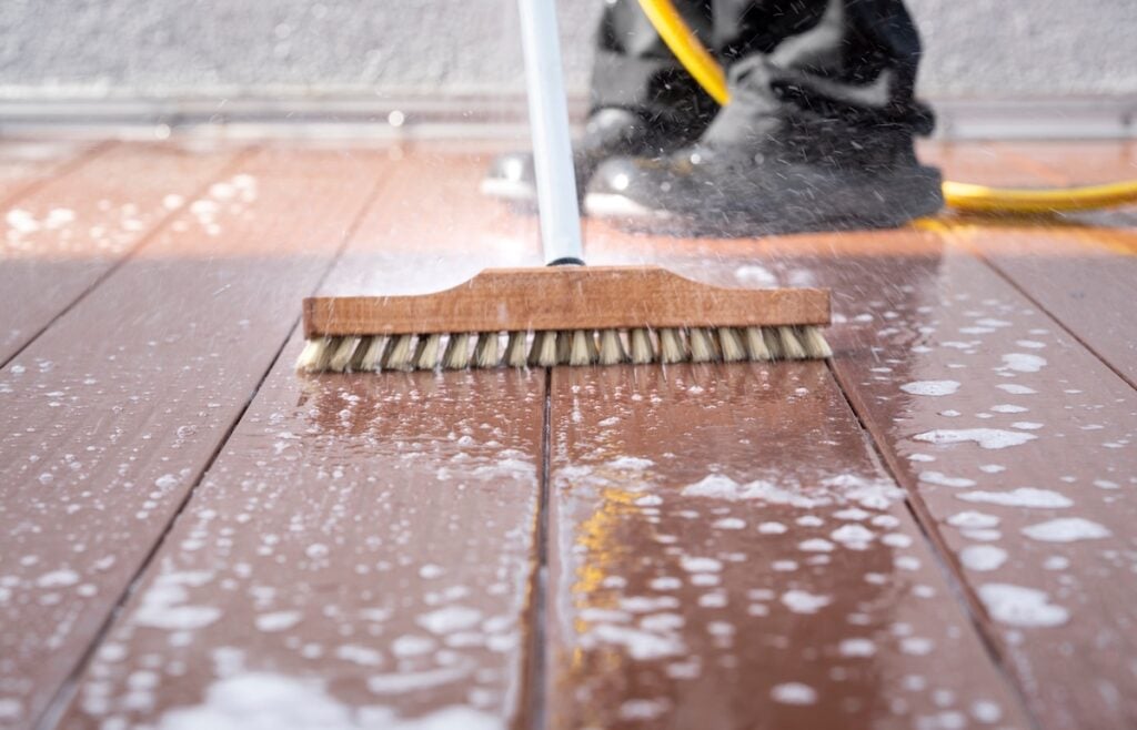 man with a scrubbing brush and a water hose scrubbing deck